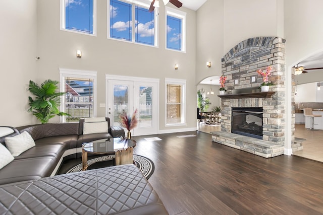 living room featuring wood finished floors, arched walkways, a fireplace, baseboards, and ceiling fan