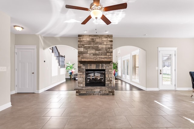 tiled living area with baseboards, arched walkways, a stone fireplace, and stairway