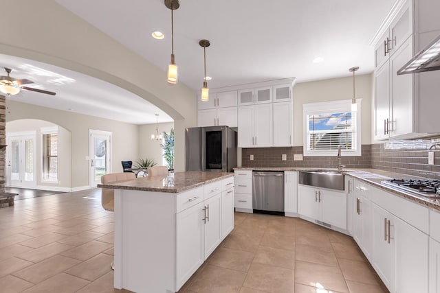 kitchen with a sink, a center island, stainless steel appliances, arched walkways, and decorative backsplash