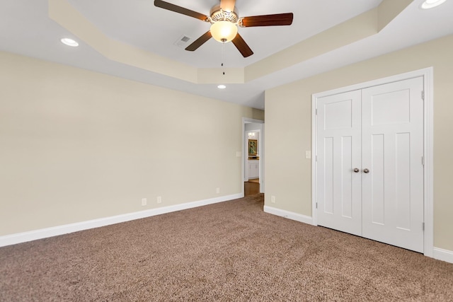 unfurnished bedroom with a raised ceiling, recessed lighting, carpet, and baseboards