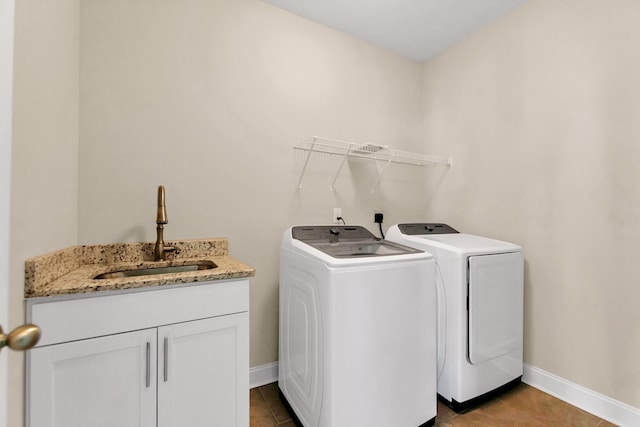 clothes washing area with a sink, washing machine and dryer, cabinet space, tile patterned flooring, and baseboards