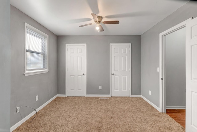 unfurnished bedroom featuring ceiling fan, light colored carpet, and multiple closets