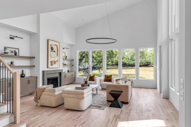 living room with a premium fireplace, high vaulted ceiling, built in features, and light wood-type flooring