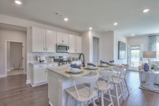 kitchen featuring dark hardwood / wood-style flooring, a center island with sink, white cabinets, and appliances with stainless steel finishes