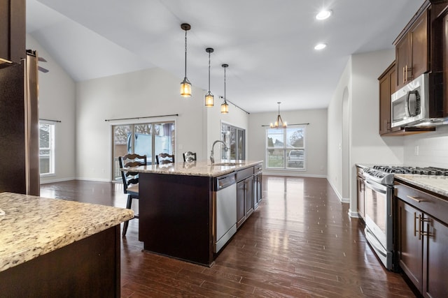 kitchen with light stone counters, an inviting chandelier, a center island with sink, appliances with stainless steel finishes, and pendant lighting