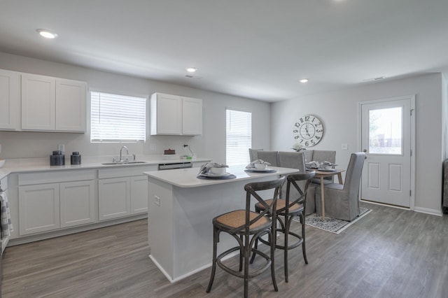 kitchen with sink, dark wood-type flooring, a breakfast bar area, white cabinets, and a kitchen island