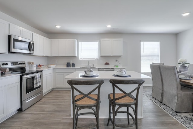 kitchen with sink, a breakfast bar area, white cabinetry, stainless steel appliances, and light wood-type flooring