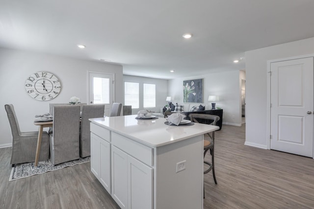 kitchen with white cabinetry, a breakfast bar, a center island, and hardwood / wood-style flooring