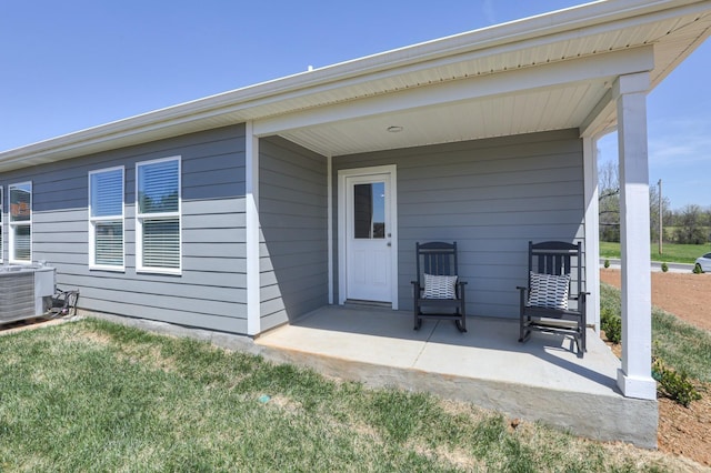 view of exterior entry featuring central AC unit, a patio area, and a lawn