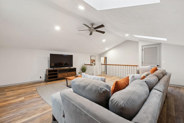 living room featuring light hardwood / wood-style flooring, ceiling fan, and vaulted ceiling with skylight