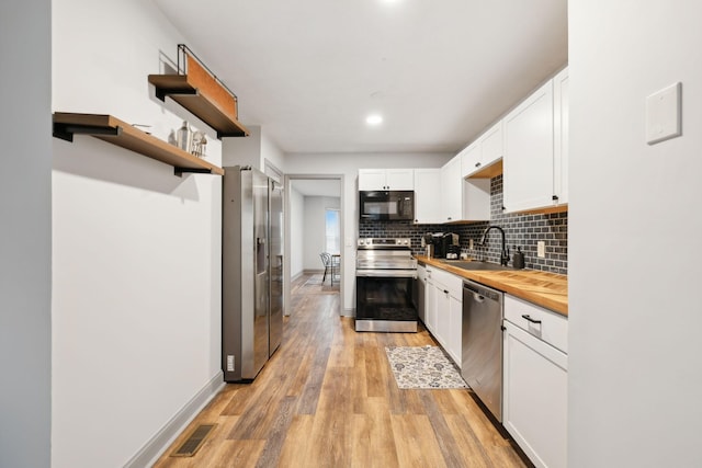 kitchen with butcher block counters, sink, light hardwood / wood-style flooring, white cabinetry, and stainless steel appliances