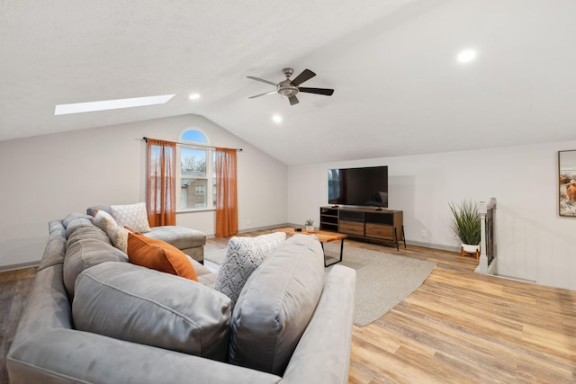 living room featuring ceiling fan, light hardwood / wood-style flooring, and vaulted ceiling with skylight