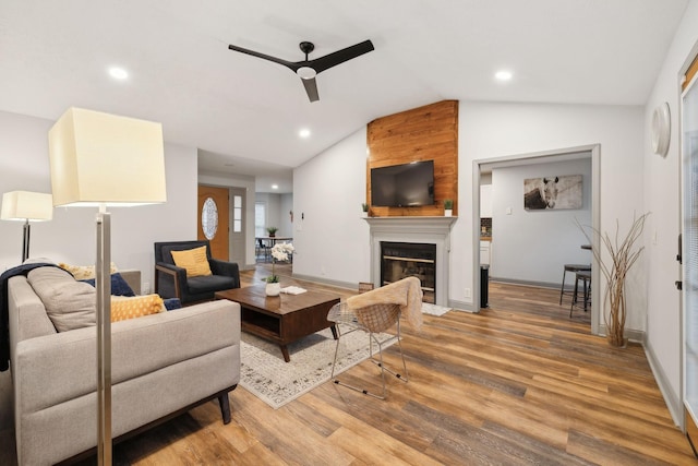 living room with ceiling fan, a large fireplace, wood-type flooring, and vaulted ceiling