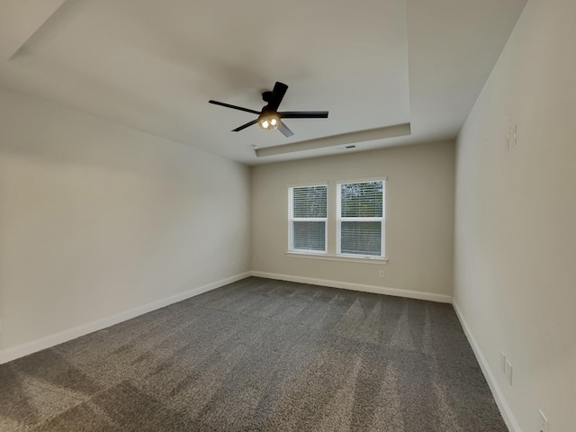 empty room with dark colored carpet, a tray ceiling, and ceiling fan