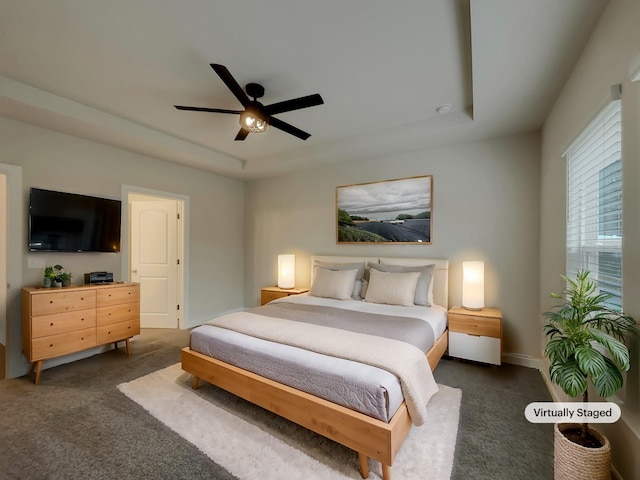 carpeted bedroom with a raised ceiling and ceiling fan