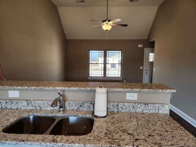 kitchen featuring light stone counters, vaulted ceiling, ceiling fan, and sink