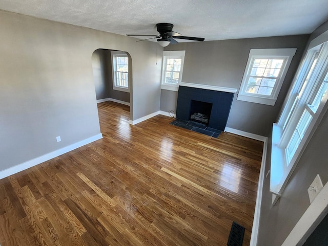 unfurnished living room with wood-type flooring, a textured ceiling, ceiling fan, and a tiled fireplace