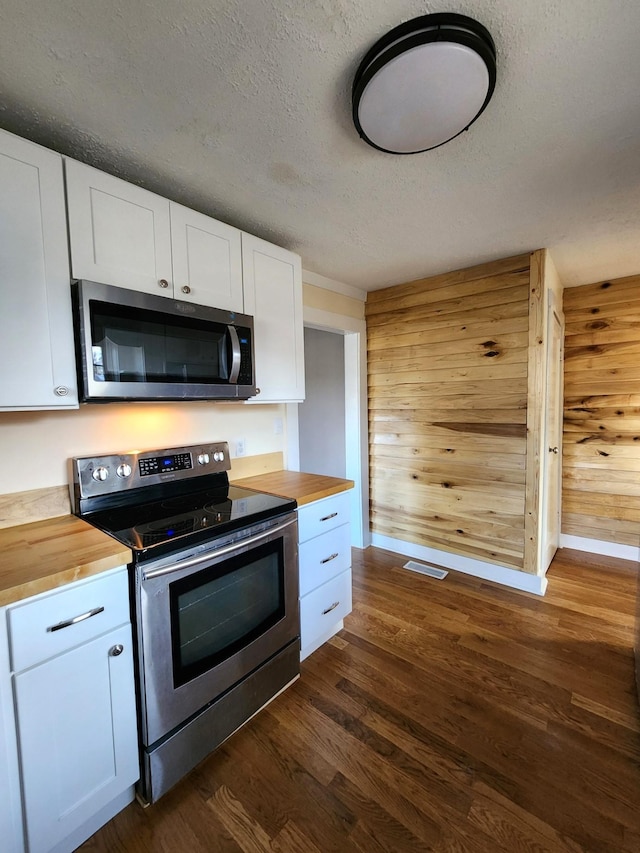 kitchen featuring stainless steel appliances, wood counters, wood walls, a textured ceiling, and white cabinets