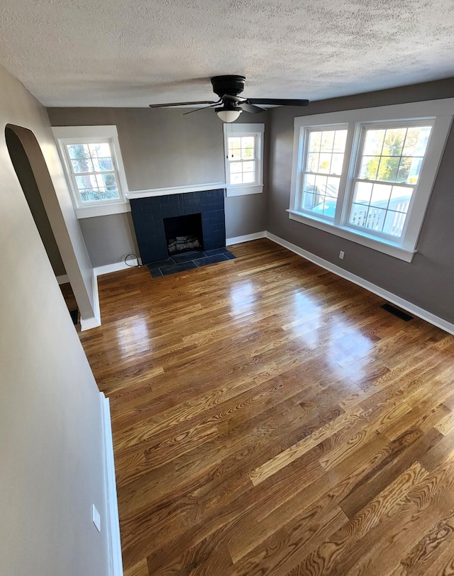 unfurnished living room featuring a textured ceiling, ceiling fan, wood-type flooring, and a fireplace