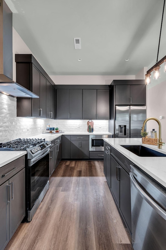 kitchen with appliances with stainless steel finishes, wall chimney exhaust hood, dark wood-type flooring, sink, and pendant lighting