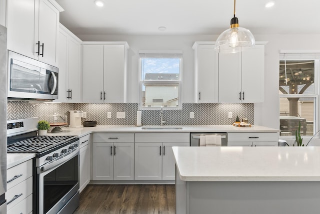 kitchen with decorative backsplash, stainless steel appliances, sink, white cabinetry, and hanging light fixtures