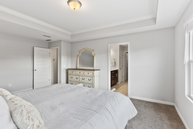 carpeted bedroom featuring a raised ceiling, crown molding, and ensuite bath