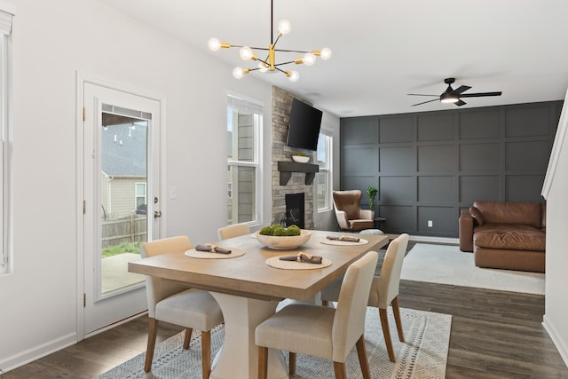 dining room with dark hardwood / wood-style flooring, a stone fireplace, and ceiling fan with notable chandelier