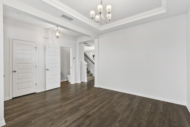 spare room with a tray ceiling, dark wood-type flooring, and a chandelier