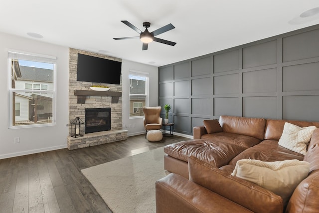 living area with a decorative wall, a fireplace, ceiling fan, and dark wood-style flooring