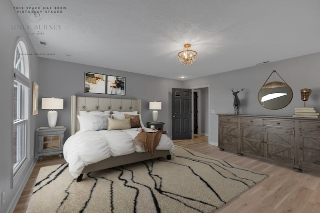 bedroom featuring multiple windows, a chandelier, light hardwood / wood-style floors, and a textured ceiling