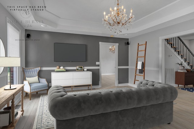 living room with a raised ceiling, a chandelier, and wood-type flooring