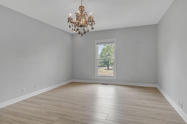 spare room featuring light hardwood / wood-style flooring and a chandelier