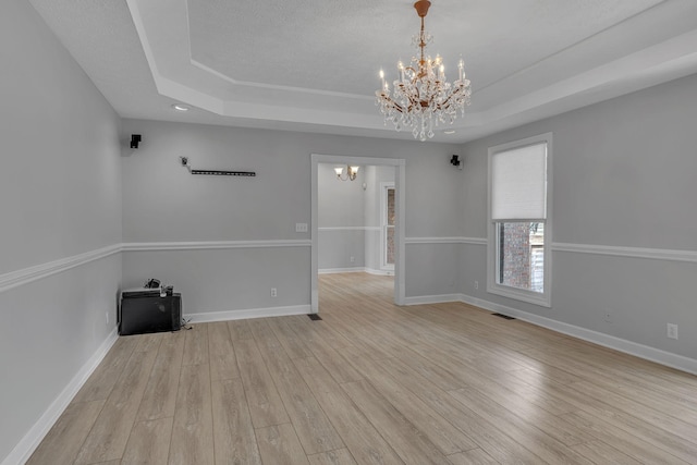 unfurnished room featuring a raised ceiling, a chandelier, and light wood-type flooring