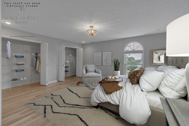 bedroom featuring a textured ceiling, light wood-type flooring, two closets, and a notable chandelier