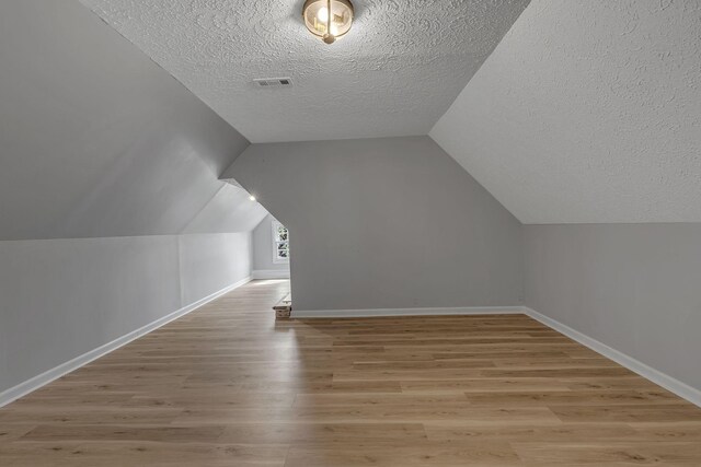 additional living space featuring lofted ceiling, light hardwood / wood-style floors, and a textured ceiling