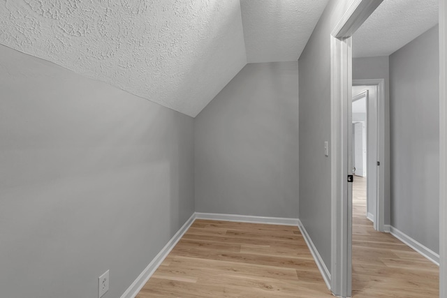 additional living space with light wood-type flooring, a textured ceiling, and vaulted ceiling