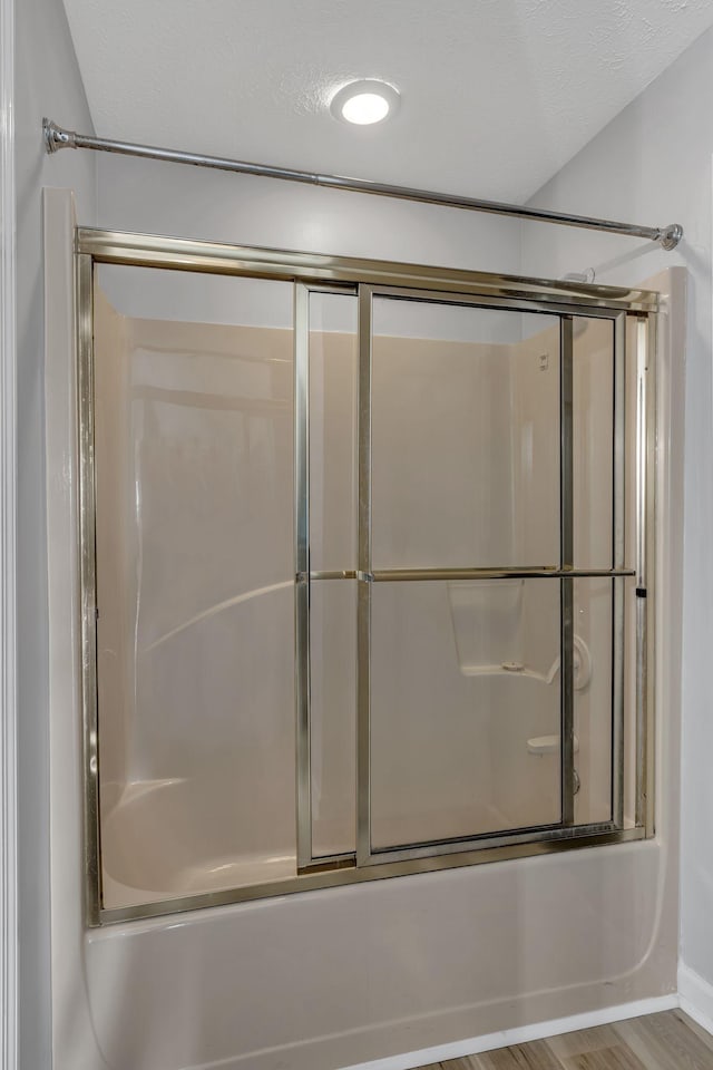 bathroom with shower / bath combination with glass door, wood-type flooring, and a textured ceiling