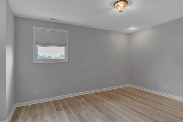 empty room with a textured ceiling and light hardwood / wood-style flooring