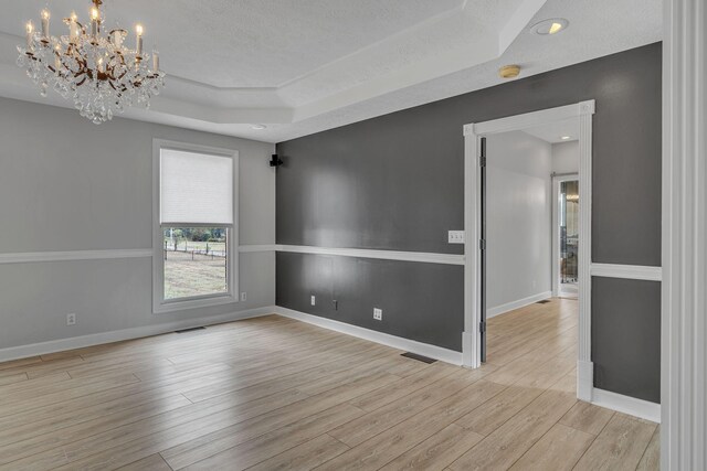 empty room featuring a raised ceiling, light wood-type flooring, a textured ceiling, and a chandelier