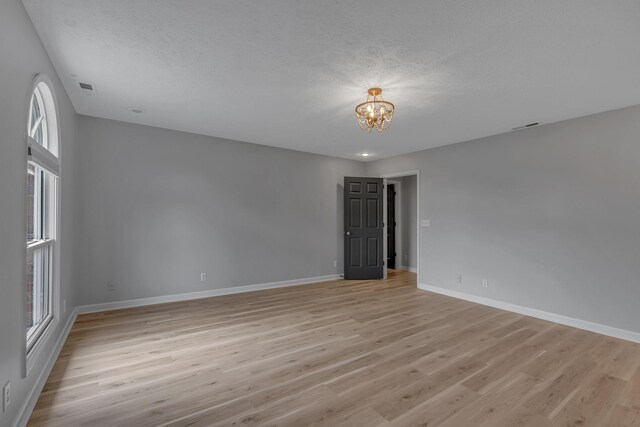 spare room featuring light hardwood / wood-style floors, a healthy amount of sunlight, a textured ceiling, and an inviting chandelier