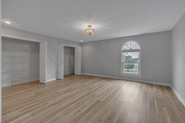 unfurnished bedroom with a textured ceiling, a chandelier, light hardwood / wood-style flooring, and multiple closets