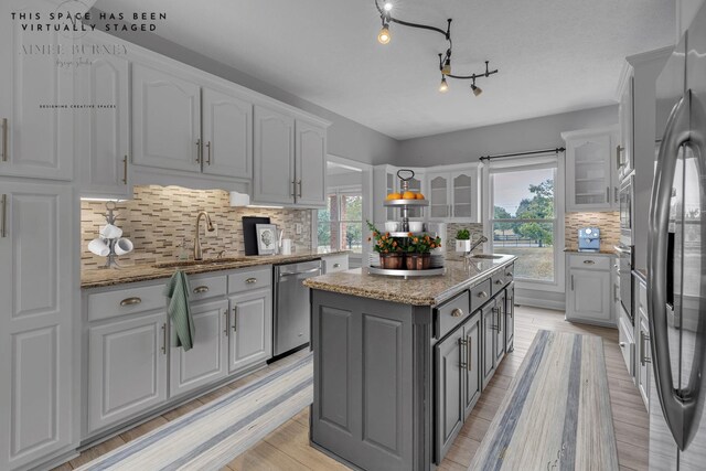 kitchen featuring decorative backsplash, light stone countertops, stainless steel appliances, sink, and a center island