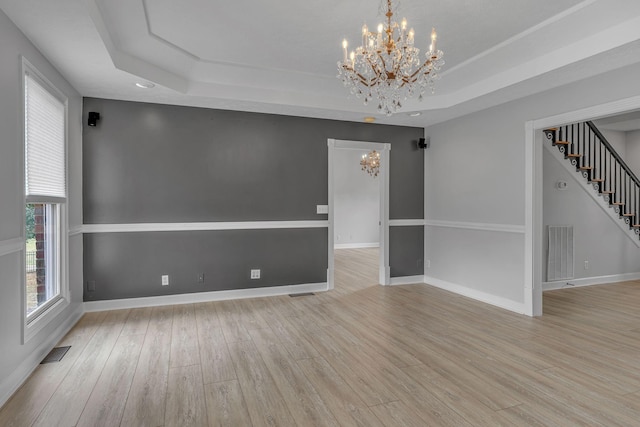 empty room with a tray ceiling, light hardwood / wood-style flooring, and a chandelier