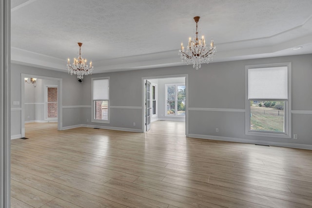 unfurnished room with a raised ceiling, a wealth of natural light, light hardwood / wood-style floors, and an inviting chandelier