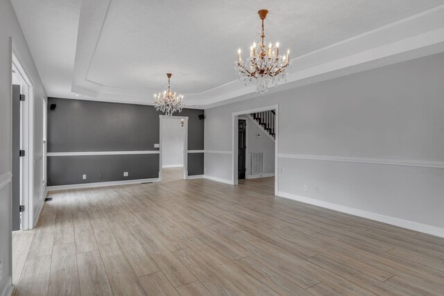 unfurnished room featuring an inviting chandelier, light hardwood / wood-style floors, and a tray ceiling