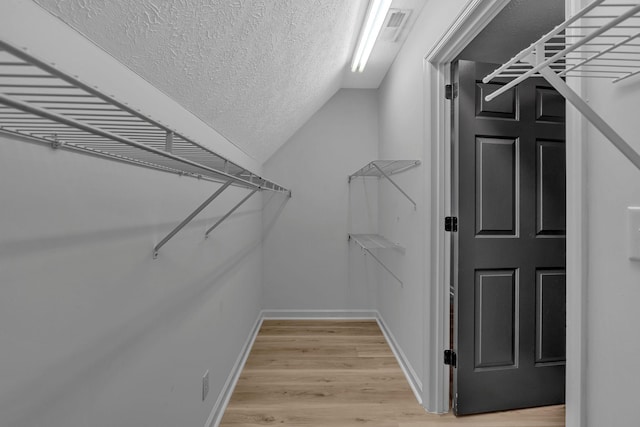 walk in closet with light hardwood / wood-style floors and vaulted ceiling