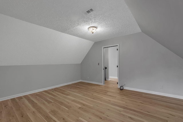 additional living space with vaulted ceiling, light hardwood / wood-style flooring, and a textured ceiling