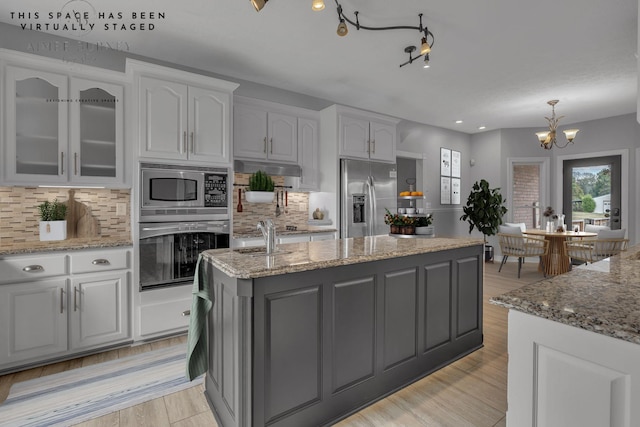 kitchen featuring decorative backsplash, stainless steel appliances, white cabinets, and an island with sink