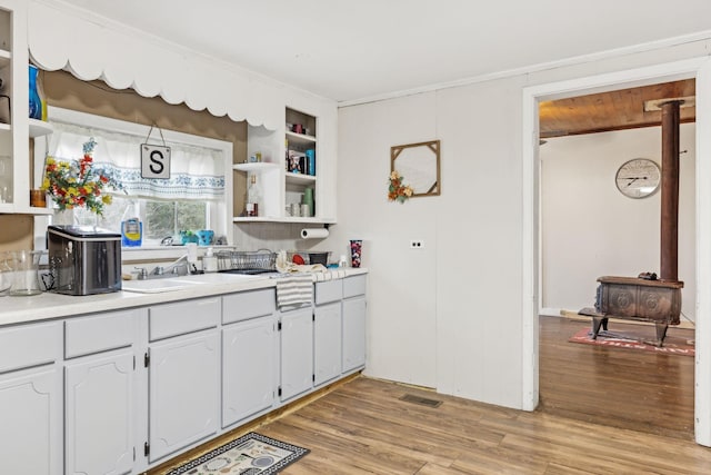 kitchen with white cabinets, light wood-type flooring, a wood stove, and sink