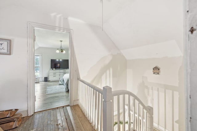 corridor with light hardwood / wood-style floors, vaulted ceiling, and a notable chandelier